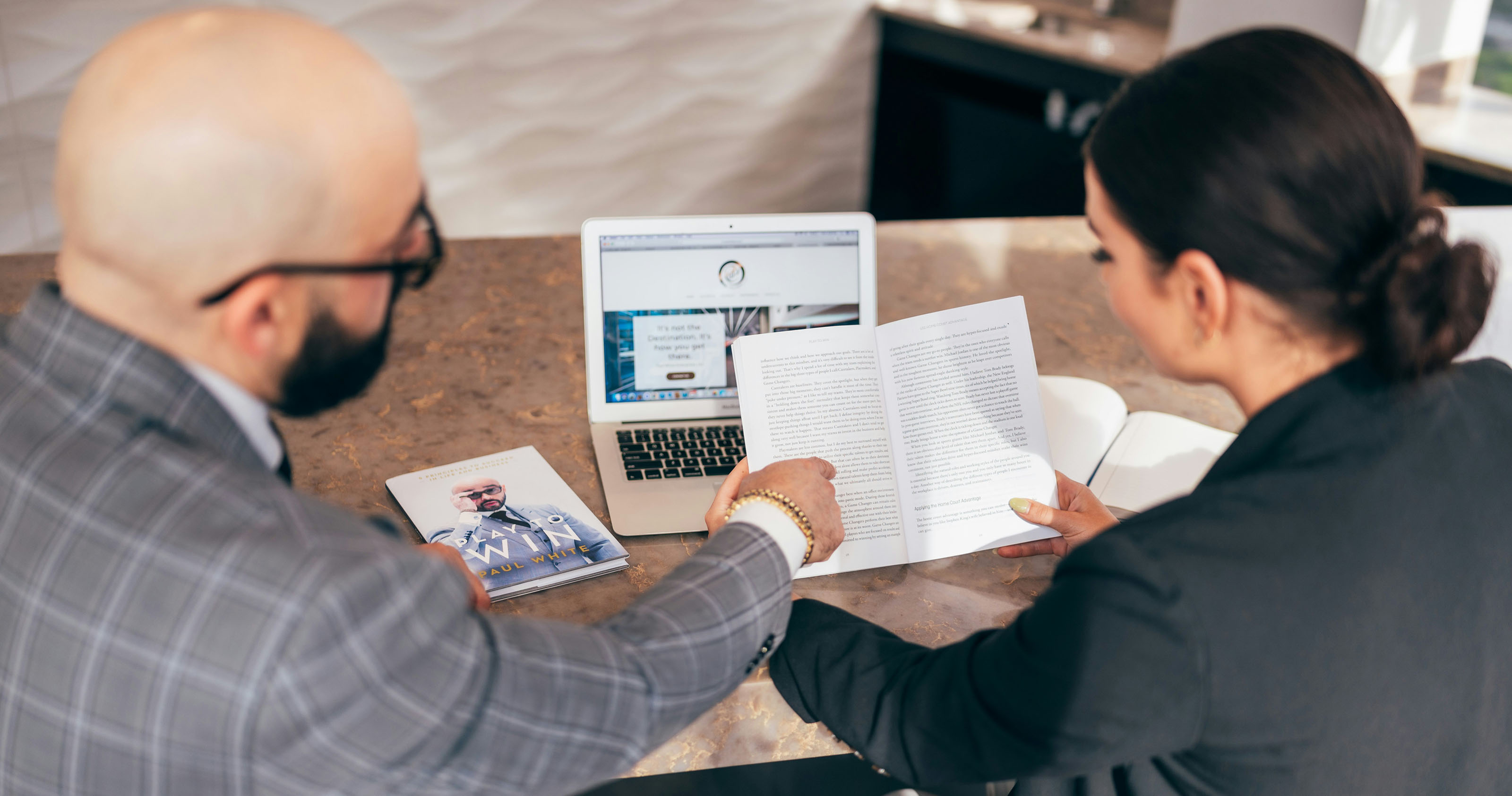 Two people talking over a computer, one pointing out a paragraph to the other.